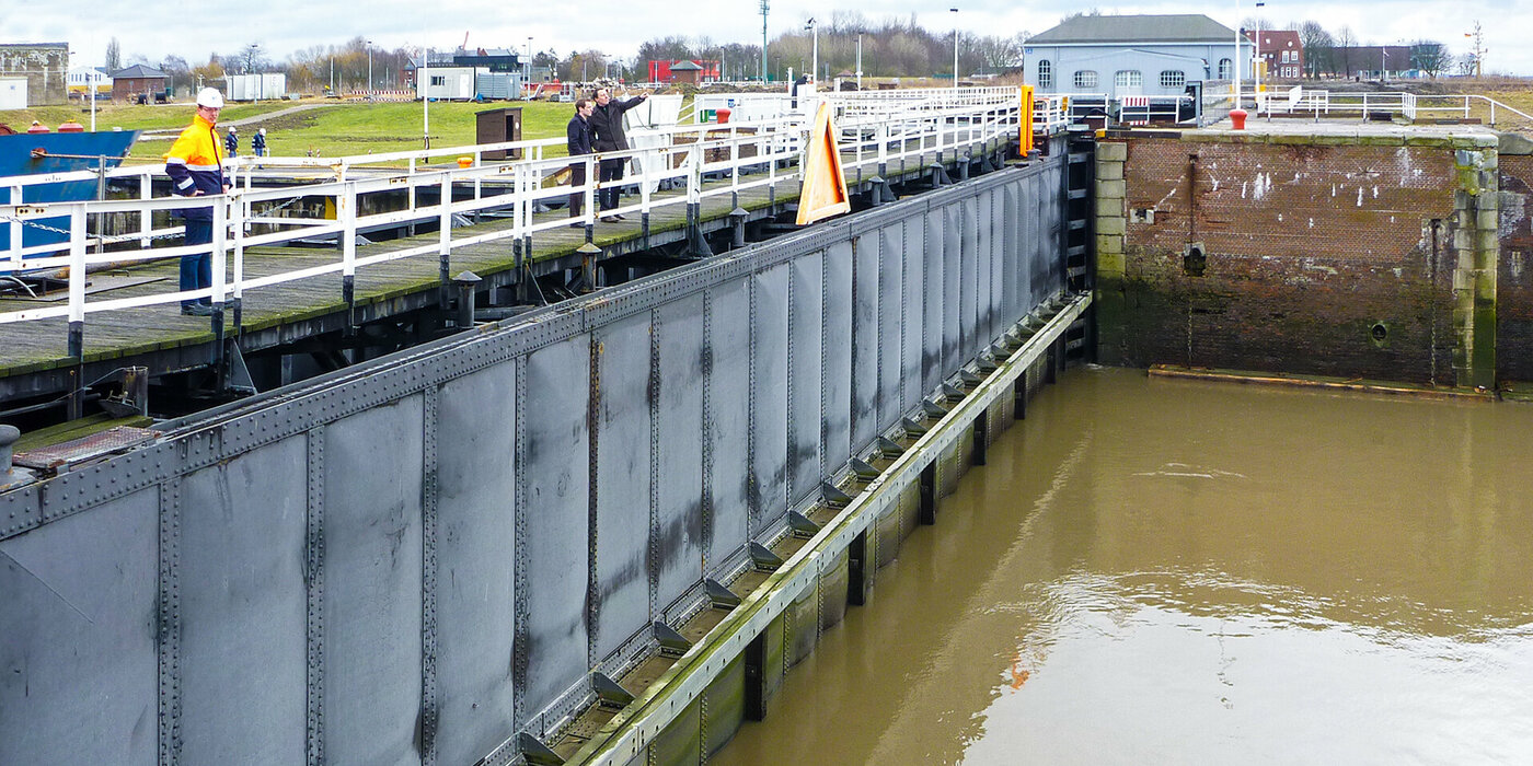 Schleusenkammer mit zwei Männern auf der Schleuse. Einer zeigt mit dem Finger in die Luft.