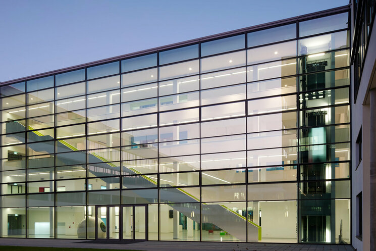 Gebäudeteil, welches nur aus Glas besteht und drinnen führt eine Treppe ins höhere Stockwerk