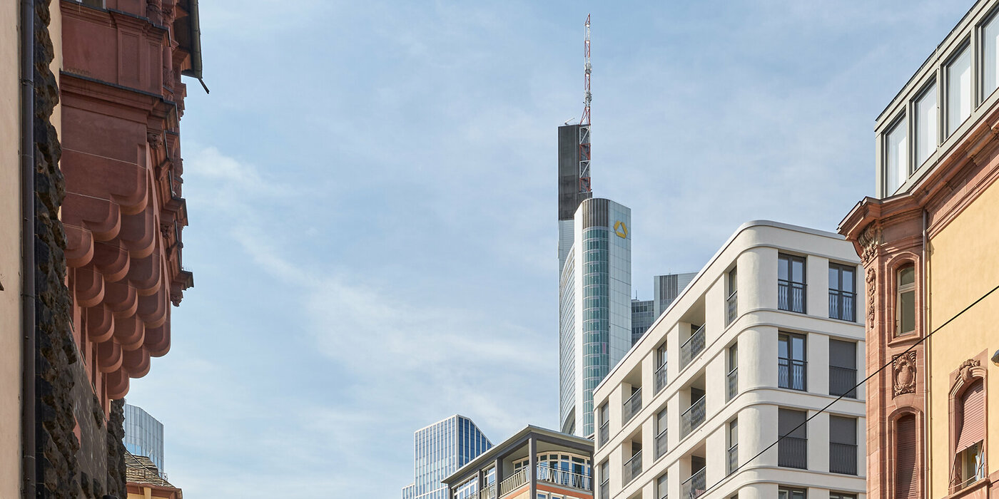 Obere Kante des Gebäudes zwischen anderen Gebäuden und im Hintergrund ist ein Hochhaus