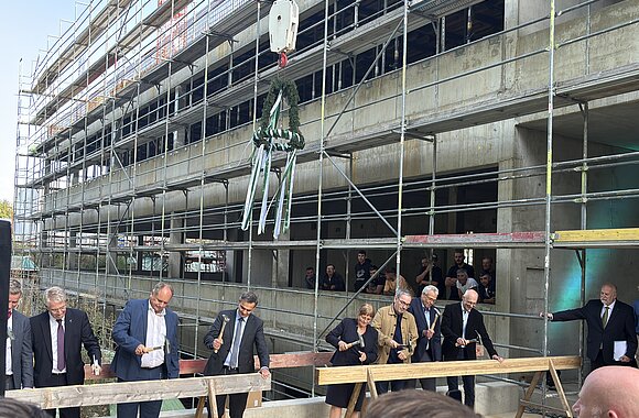 Traditioneller Nageleinschlag beim Richtfest mit Richtkranz.  Von links: Dr.-Ing. E. h. Thomas Reiter, Abteilungsleiter für Raumfahrt und Sicherheit im Bundesministerium für Forschung, Technologie und Raumfahrt; Dirk Hilbert, Oberbürgermeister der Landeshauptstadt Dresden; Falk Reinhardt, Technischer Geschäftsführer des Staatsbetriebs Sächsisches Immobilien- und Baumanagement; Juliane Schmidt, Kaufmännische Direktorin des IFW Dresden; Jan Gerken, Kanzler der TU Dresden; Prof. Dr. Bernd Büchner, Wissenschaftlicher Direktor des IFW Dresden, und Prof. Dr. Matthias Vojta, Sprecher des Exzellenzclusters ctd.qmat.