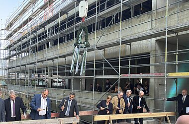 Traditioneller Nageleinschlag beim Richtfest mit Richtkranz. Von links: Dr.-Ing. E. h. Thomas Reiter, Abteilungsleiter für Raumfahrt und Sicherheit im Bundesministerium für Forschung, Technologie und Raumfahrt; Dirk Hilbert, Oberbürgermeister der Landeshauptstadt Dresden; Falk Reinhardt, Technischer Geschäftsführer des Staatsbetriebs Sächsisches Immobilien- und Baumanagement; Juliane Schmidt, Kaufmännische Direktorin des IFW Dresden; Jan Gerken, Kanzler der TU Dresden; Prof. Dr. Bernd Büchner, Wissenschaftlicher Direktor des IFW Dresden, und Prof. Dr. Matthias Vojta, Sprecher des Exzellenzclusters ctd.qmat.