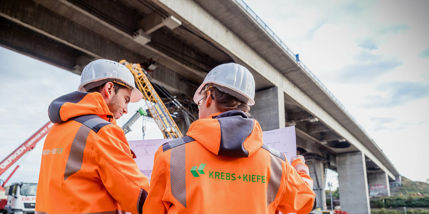 Zwei Krebs und Kiefer Mitarbeiter stehen vor einer Brücke und lesen einen Plan